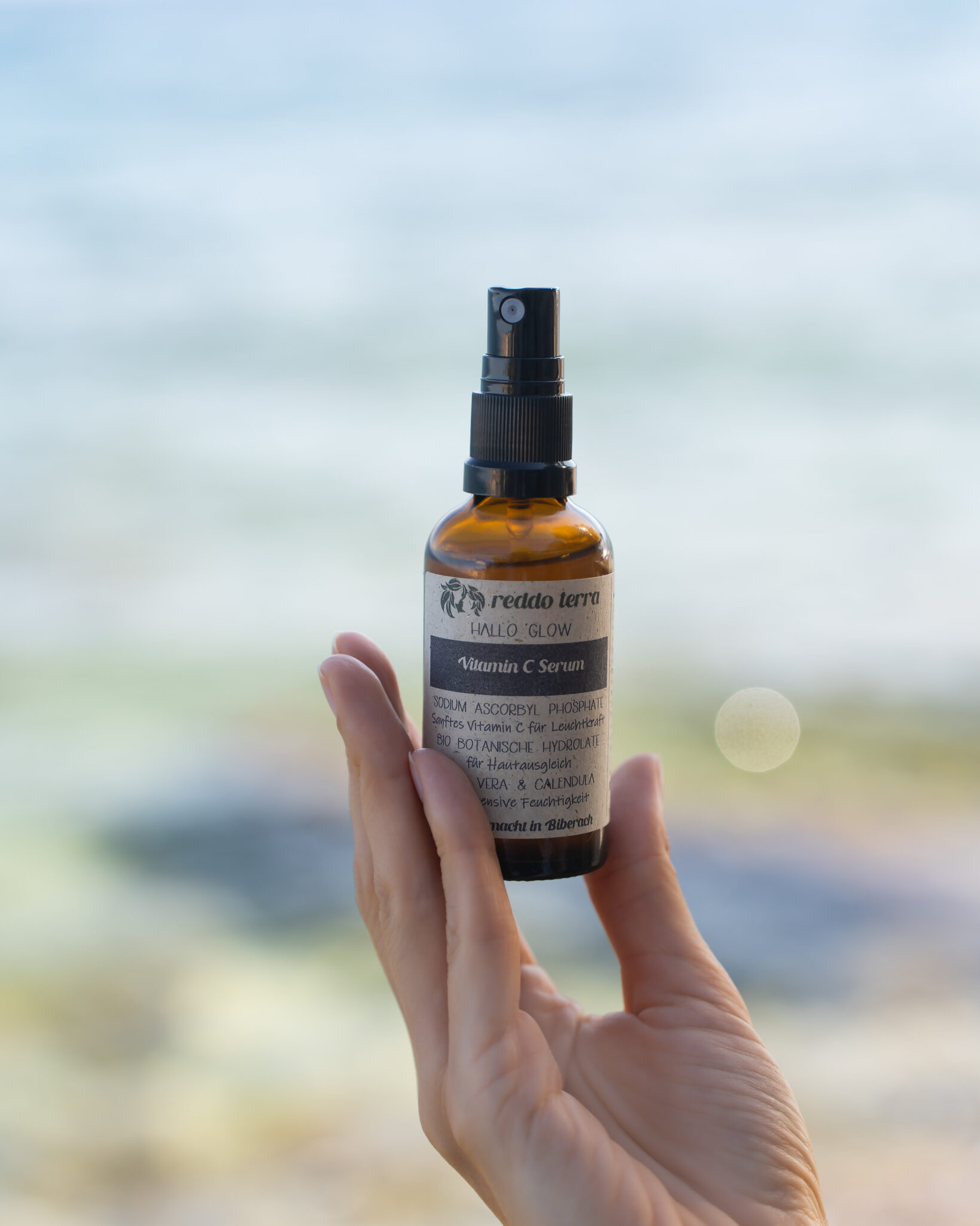 Hallo Glow Vitamin C Serum in der Hand am Meer